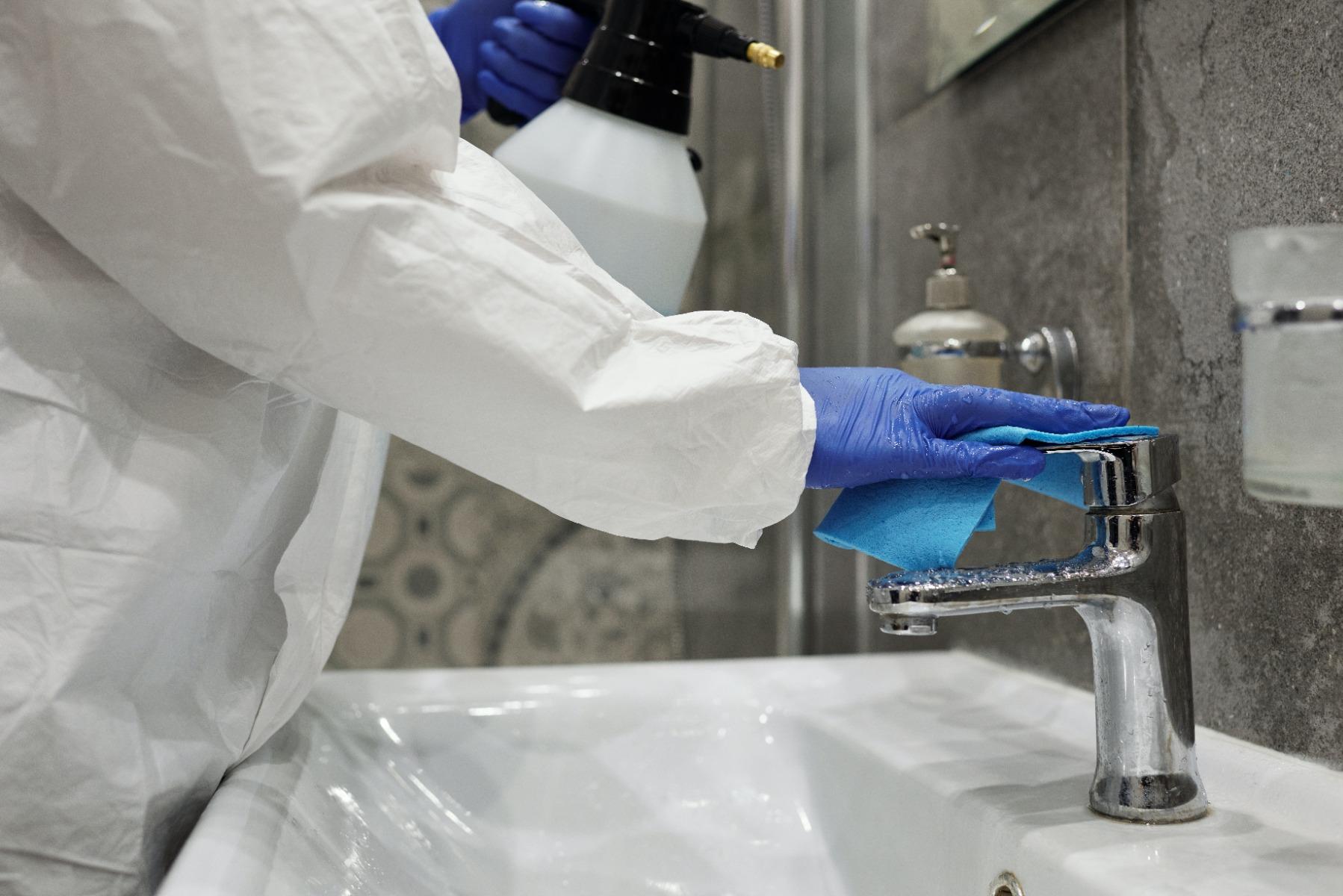 someone wearing gloves cleaning a sink with a wet cloth and spray